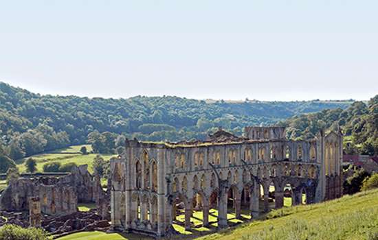 Looking down a grassy hill to the tall ruins of Rievaulx Abbey