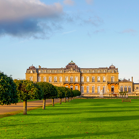 Looking across lawns to the large French-looking country house (Wrest Park) which looks amber in the evening sun